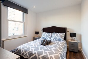 Une chambre à coucher bien aménagée, avec un grand lit, deux tables de chevet et une fenêtre donnant sur les bâtiments environnants.