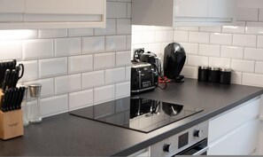 Une cuisine moderne avec des carreaux de céramique blancs disposés en motif métro, une plaque de cuisson à induction noire, une machine à café et un ensemble de couteaux.