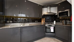 A modern kitchen with dark cabinetry, a stainless steel sink, a built-in oven, and a microwave. - Central London 3 Bed Flat FS4 (London)