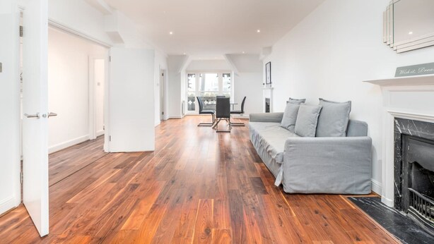 A spacious living room with a grey sofa, a fireplace, and a wooden floor. - Central London 3 Bed Flat FS4 (London)