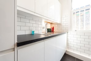 Eine moderne Küche mit weißen Schränken, einer schwarzen Arbeitsplatte und einem Fenster mit Blick auf eine Backsteinmauer.