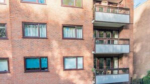 Een meerlaags bakstenen gebouw met balkons, een omheinde tuin en een heldere lucht.