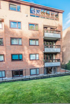 A multi-story brick building with balconies, a fenced yard, and a clear sky. - Stylish Two Bedroom Flat BCA (London)