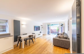 A modern living space with a dining area, a sofa, a TV, and a sliding glass door leading to an outdoor area. - Stylish Two Bedroom Flat BCA (London)