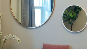 Ein rosafarbenes Sofa mit vielen Kissen, ein großer runder Spiegel an der Wand und ein kleinerer Spiegel darunter.
