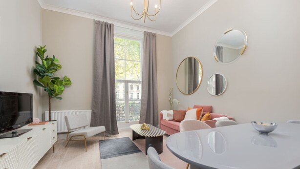 Ein modernes Wohnzimmer mit Fernseher, Sofa, Esstisch und großen Fenstern.