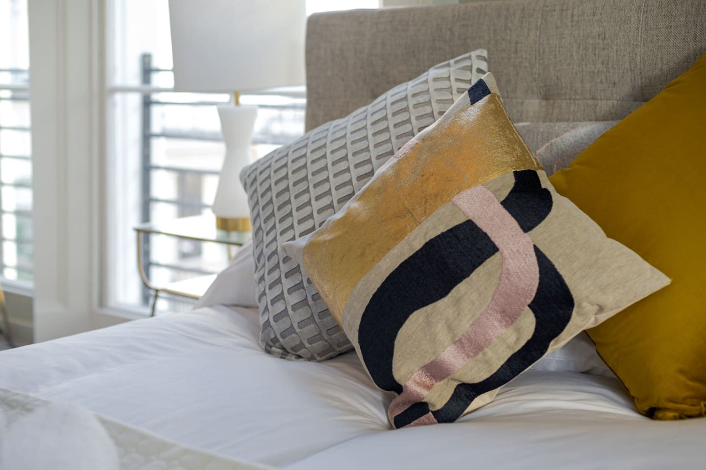 A neatly made bed with a white comforter and several pillows, including a geometric patterned one and a striped one.