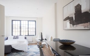 A modern hotel room with a bed, a dining area, and a large abstract painting on the wall. - Cool Kings Cross Apartment OM5 (London)