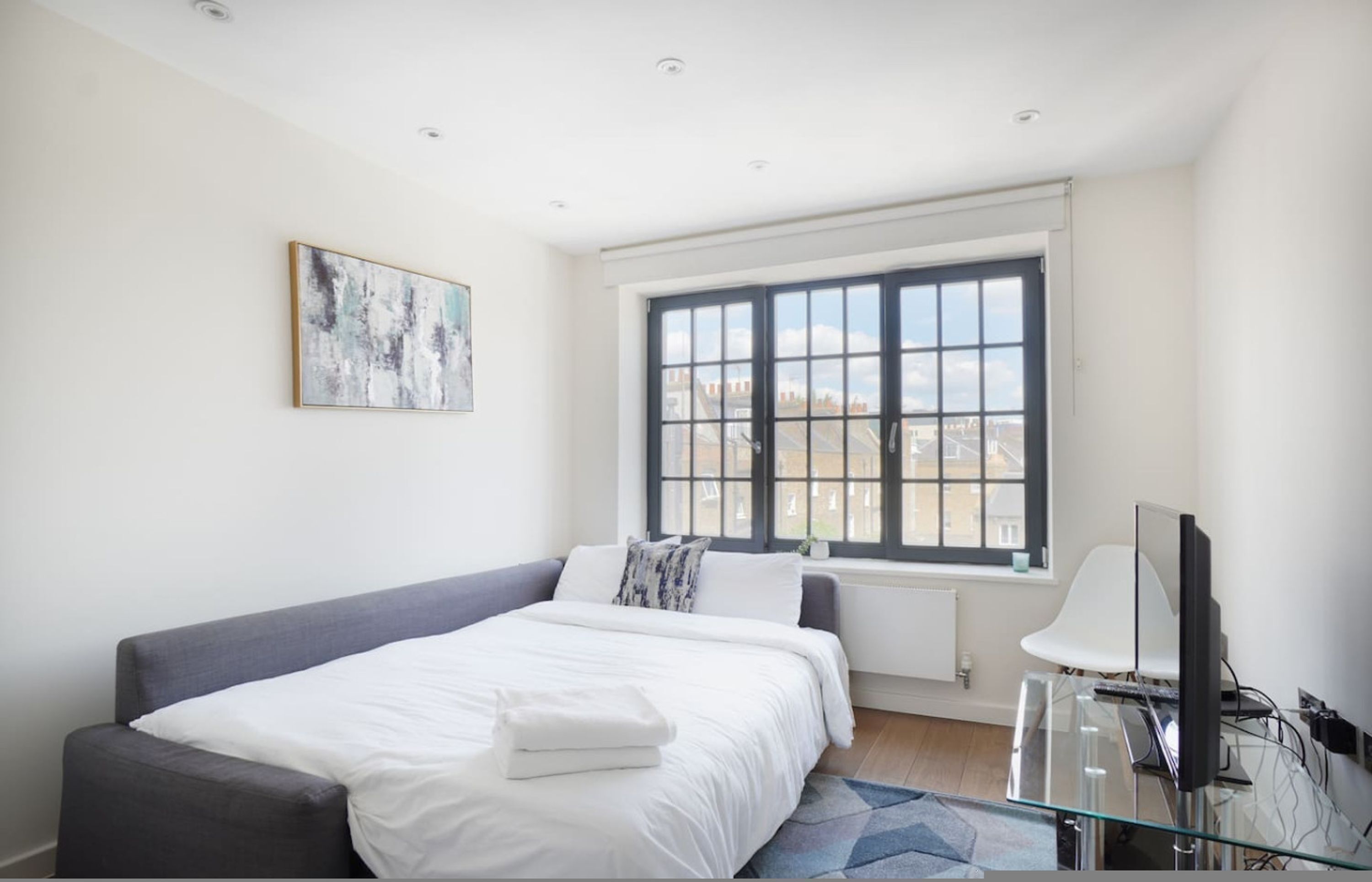 Une chambre moderne avec un grand lit, une fenêtre donnant sur la ville, un téléviseur à écran plat et un tableau accroché au mur.