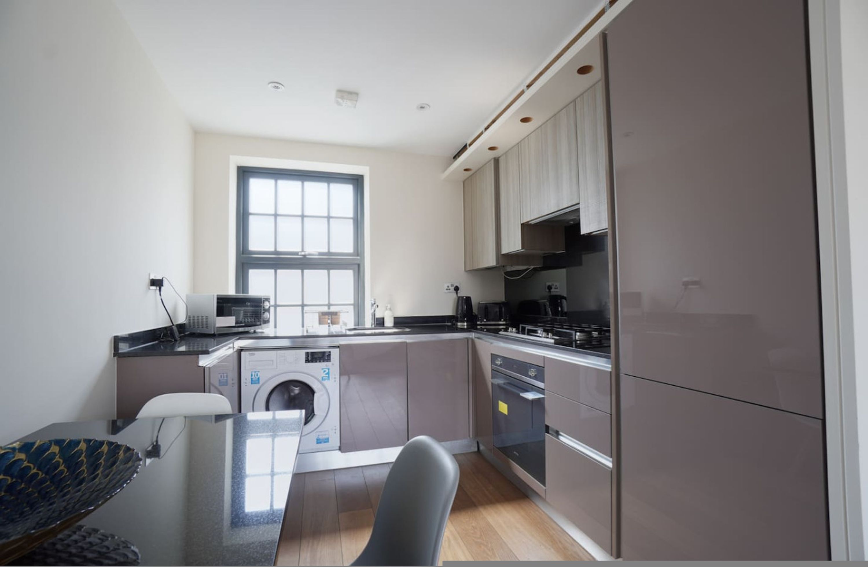 A modern kitchen with a built-in washer and dryer, a large window, and a dining area with a table and chairs.