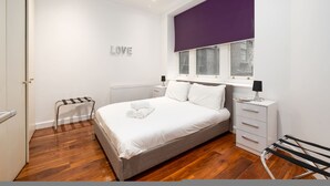 A modern bedroom with a bed, a nightstand, a radiator, a window with a purple blind, and a wall-mounted sign that says "LOVE". - Central London Flat FS1 (London)
