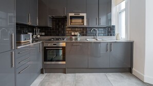 A modern kitchen with dark cabinets, stainless steel appliances, and a large window. - Central London Flat FS1 (London)