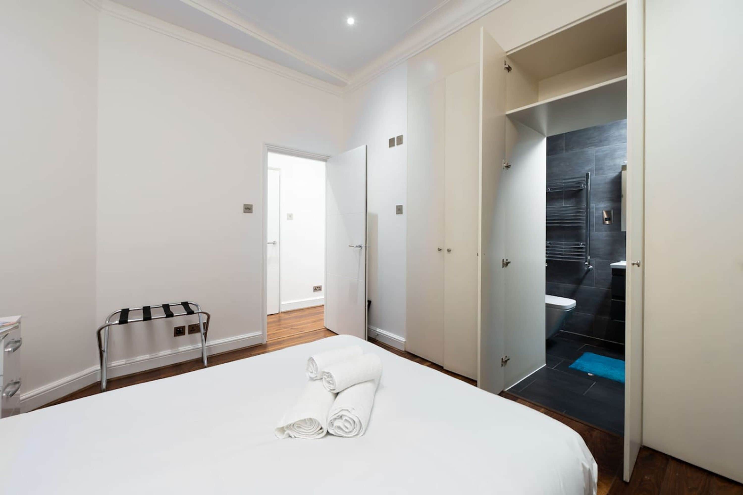 Ein Hotelzimmer mit Bett, Handtuchhalter, einer Tür zu einem Badezimmer und Blick ins Badezimmer.