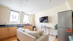 A compact kitchen with wooden cabinets, a sofa, a TV, and a refrigerator. - Stylish 3 Bedroom Flat CRC (London)