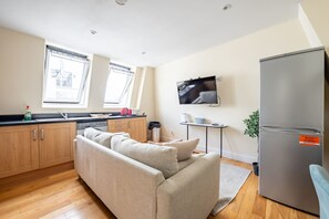 A compact kitchen with wooden cabinets, a sofa, a TV, and a refrigerator. - Stylish 3 Bedroom Flat CRC (London)