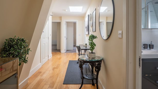 A hallway with a staircase, a dining area with a table and chairs, and a potted plant. - Stylish 3 Bedroom Flat CRC (London)