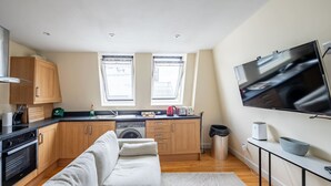 A modern kitchen with wooden cabinets, a built-in oven, and a large window. - Stylish 3 Bedroom Flat CRC (London)