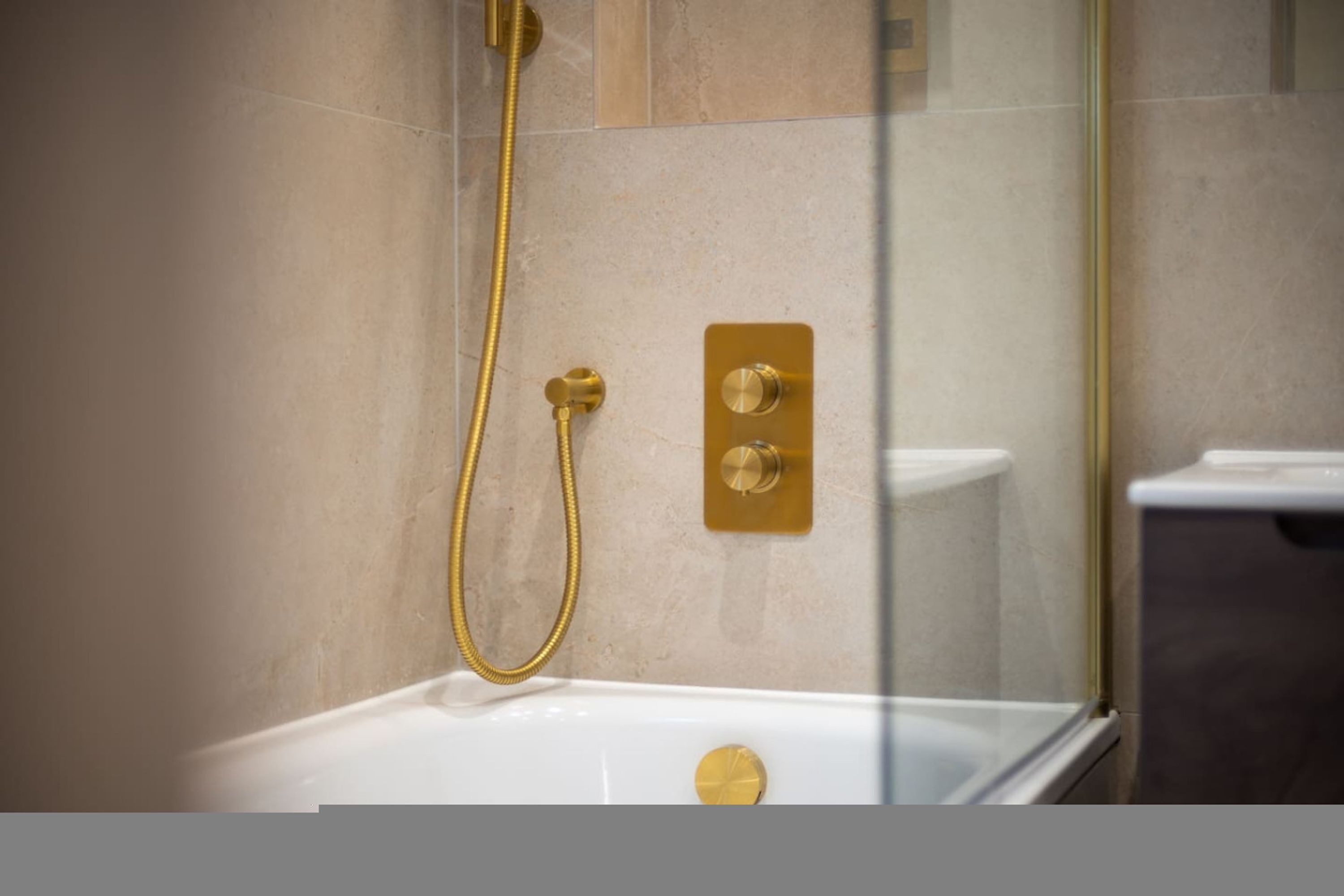 A modern bathroom with a glass-enclosed shower, a white bathtub, and gold fixtures.