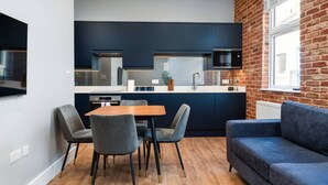 A modern kitchen with dark cabinets, a wooden dining table, and a blue sofa. - Trendy Islington Flat Us74 (London)