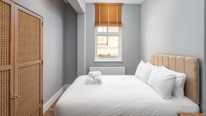 A bedroom with a large bed, a window with blinds, a radiator, and a wooden wardrobe. - Trendy Islington Flat Us74 (London)