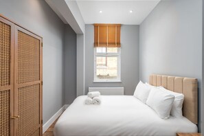A bedroom with a large bed, a window with blinds, a radiator, and a wooden wardrobe. - Trendy Islington Flat Us74 (London)