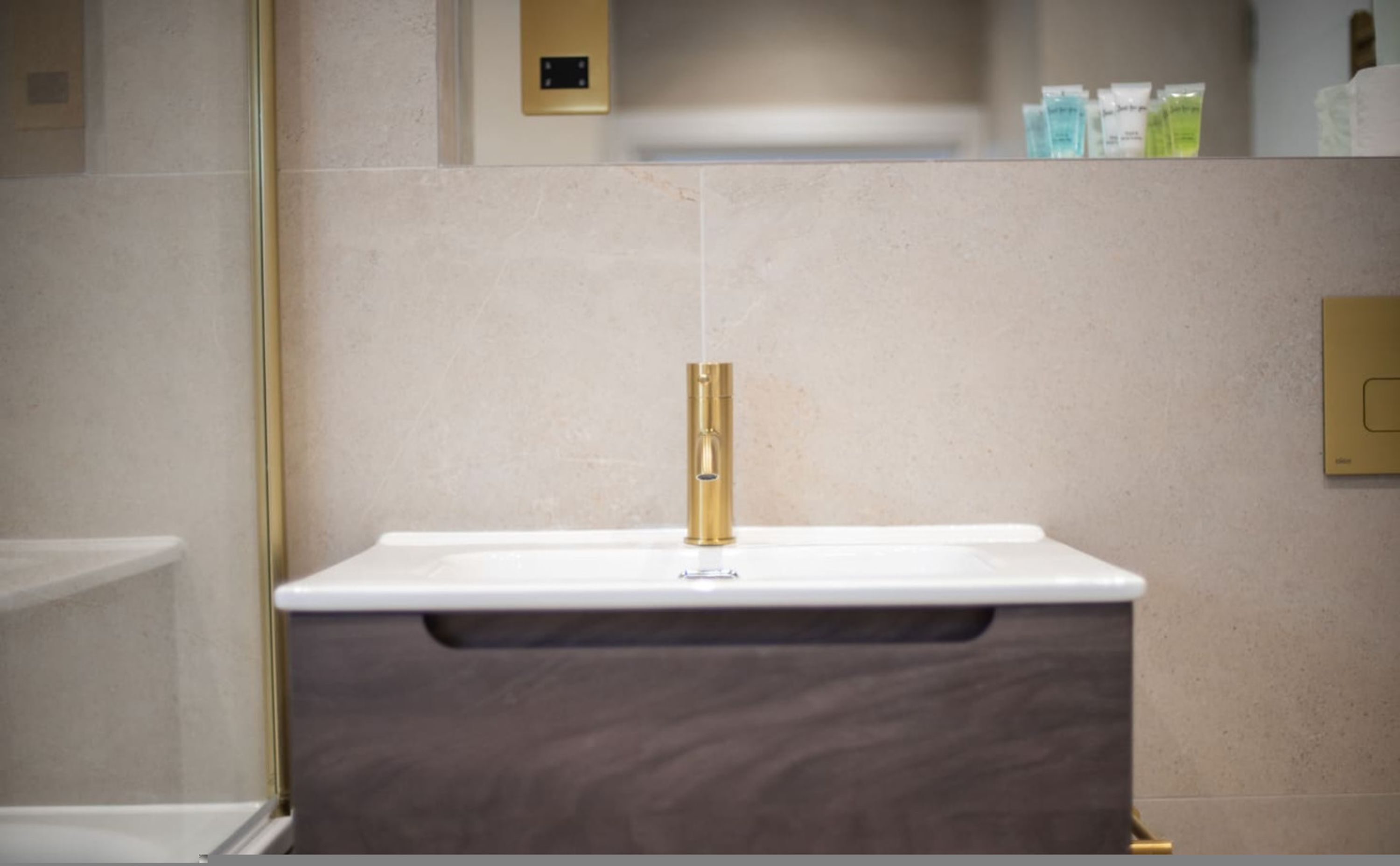Un baño moderno con lavamanos blanco, grifo dorado y tocador de madera oscura.