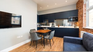 A modern kitchen with dark cabinets, a wooden dining table, and a blue sofa. - Trendy Islington Flat Us74 (London)