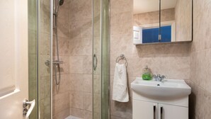 Een badkamer met een douche met glazen wanden, een witte wastafel en een spiegel boven de wastafel.