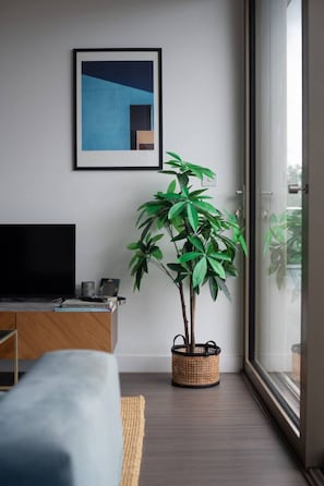 Ein modernes Wohnzimmer mit großem Fenster, Flachbildfernseher, einer Couch, einem Topf mit Pflanze und einem gerahmten Kunstwerk an der Wand.