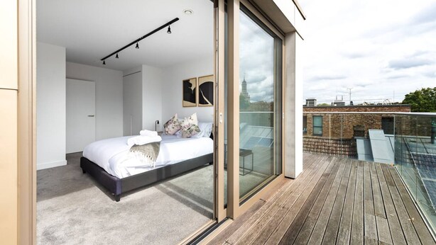 Una camera da letto moderna con un letto grande, una porta vetrata che dà su un balcone e vista sulla città.