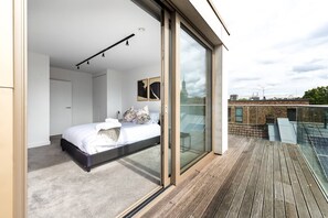 A modern bedroom with a large bed, a glass door leading to a balcony, and a city view. - Modern 1-bedroom Flat Cre8 (London)