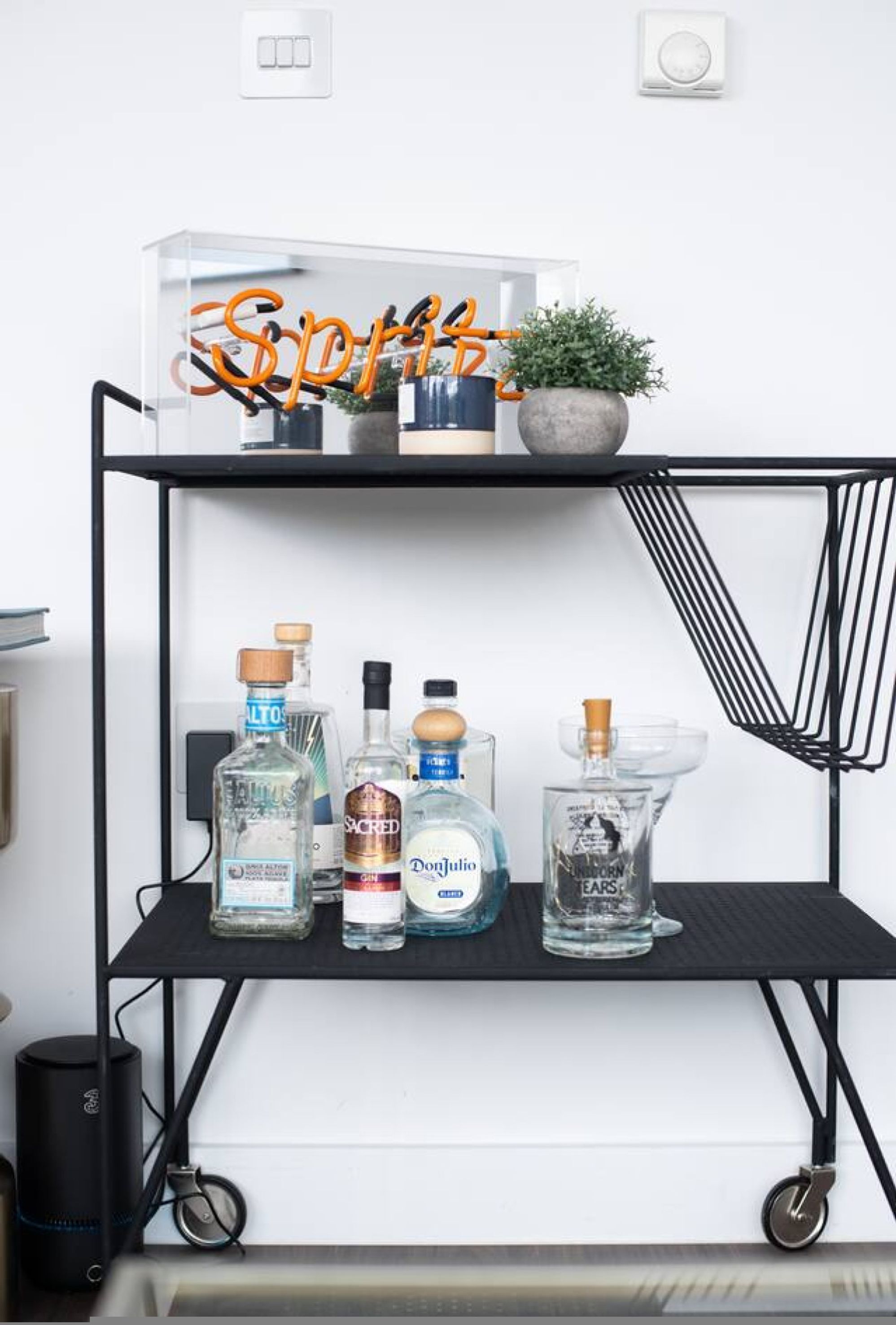 A black metal shelf with various bottles of alcohol and a potted plant.