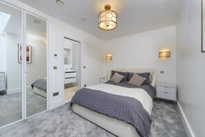 A bedroom with a large bed, bedside tables, a wardrobe, and a mirror. - Gorgeous Hampstead Home (London)