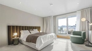 Ein modernes Hotelzimmer mit einem großen Bett, einem Nachttisch, einem grünen Sessel und Blick auf die Stadt durch große Fenster.