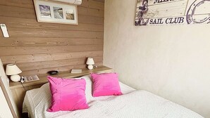 Une chambre avec une tête de lit en bois, un lit avec des oreillers roses, une table de chevet avec une lampe et un panneau mural sur lequel on peut lire : « MARINE SAIL CLUB ».