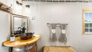 Une salle de bain rustique avec un lavabo en forme de tonneau en bois, un grand miroir et un porte-serviettes avec deux serviettes.