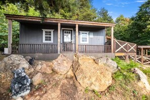 Uma cabana com varanda, deck de madeira e grandes pedras na frente.