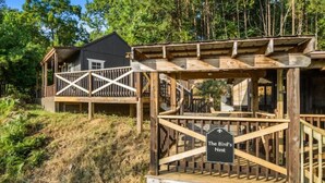 Une terrasse en bois, sur laquelle est fixée une pancarte indiquant « Le Nid d’Oiseau », mène à un chalet.