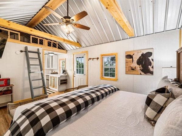 Quarto com cama, escada, ventilador de teto e um quadro na parede.