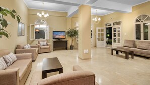 A spacious living room with beige walls, a flat-screen TV, and a large potted plant. - PLATY BEACH HOTEL (Lemnos)