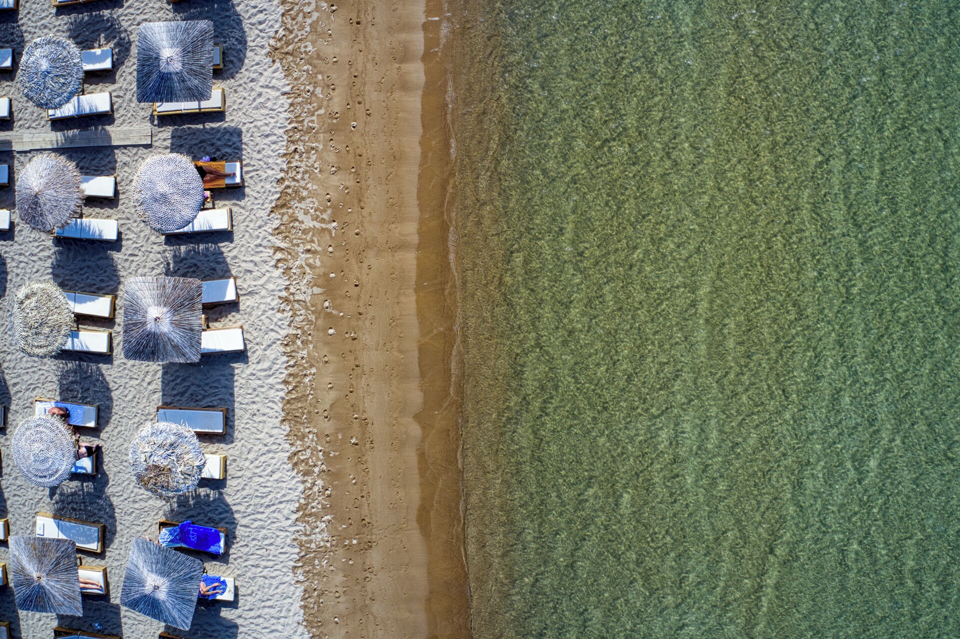 An aerial view of a beach with rows of umbrellas and lounge chairs, indicating a beach resort setting.