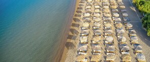 Oversigtsbillede af en strand med rækker af liggestole og stråparasoller.