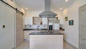 Une cuisine moderne dotée d’un îlot central, de meubles blancs et d’une hotte de cuisine en acier inoxydable.