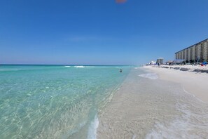 A beach with clear turquoise water, a sandy shore, and a hotel building in the background. - Coastal Retreat | Walk to Beach | Designer Yard (Panama City)