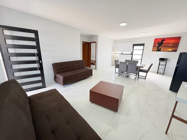 A modern living room with a sofa, a coffee table, and a dining area with chairs and a table.
