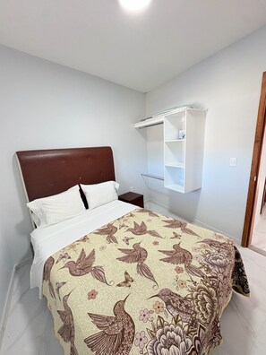 Ein Schlafzimmer mit einem Bett, weißen Wänden, einem Holzkopfteil, einem weißen Nachttisch und einem weißen Kleiderschrank.