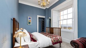 A bedroom with a bed, a nightstand, a lamp, a chair, a window, and a door. - Elegant 3-Bed Flat | Near Free Parking & Hill View (Stirling)