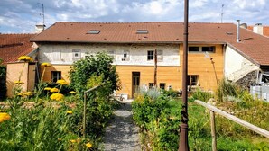 A traditional European-style building with a tiled roof, a central entrance, and a garden with yellow flowers.