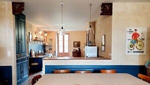 A dining area with a large table and wooden chairs, a kitchen with wooden cabinets and a refrigerator, and a poster on the wall.