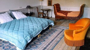 A bedroom with a large bed, a small table, a chair, and a rug.